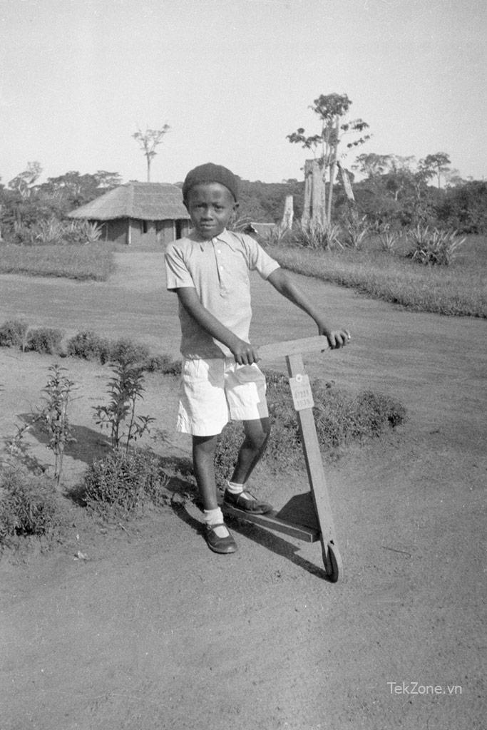 Cậu bé da đen trên chiếc xe tay ga bằng gỗ, trong khung cảnh nông thôn.