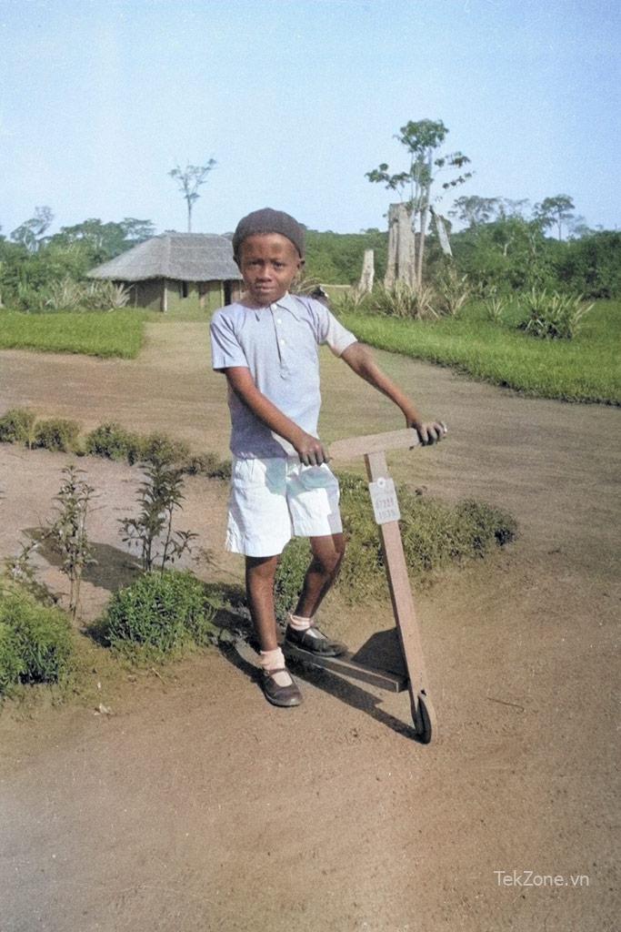 Cậu bé da đen tạo dáng trên chiếc xe tay ga bằng gỗ trong khung cảnh nông thôn xanh tươi.  Ví dụ tô màu Photoshop AI