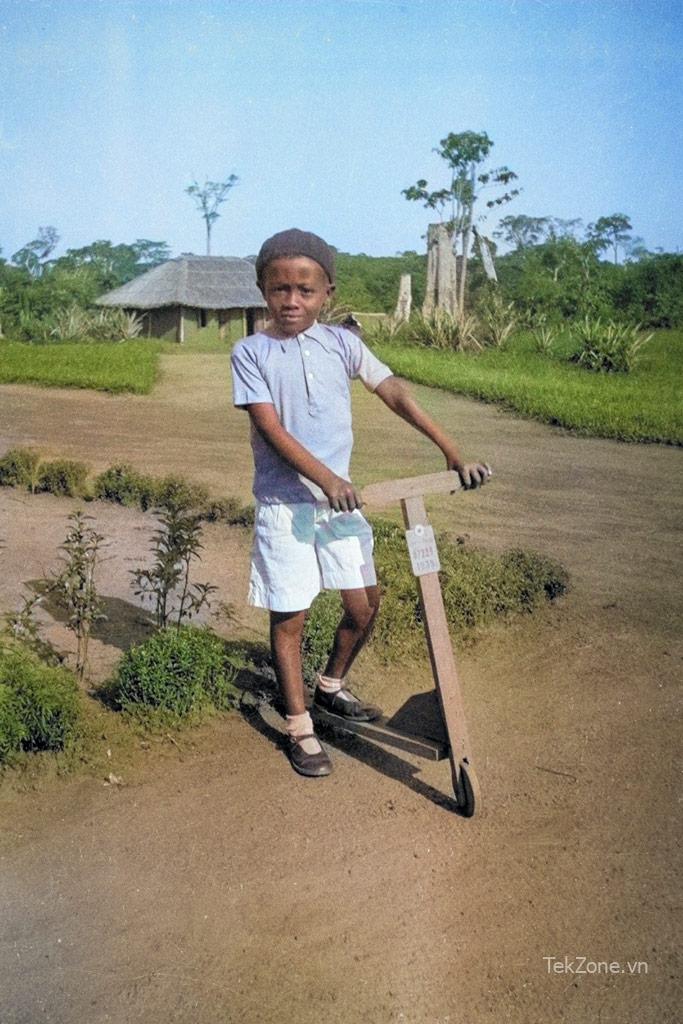 Cậu bé da đen tạo dáng trên chiếc xe tay ga bằng gỗ trong khung cảnh nông thôn xanh tươi.  Ví dụ tô màu Photoshop AI